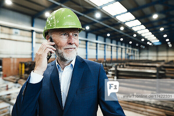 Businessman with hardhat talking on mobile phone in industry