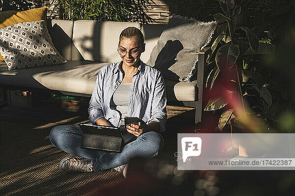 Smiling businesswoman using mobile phone and digital tablet on terrace