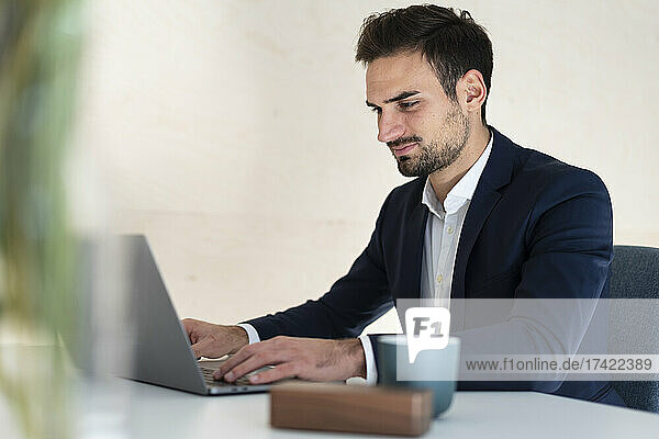 Young businessman typing on laptop while sitting at desk working in office