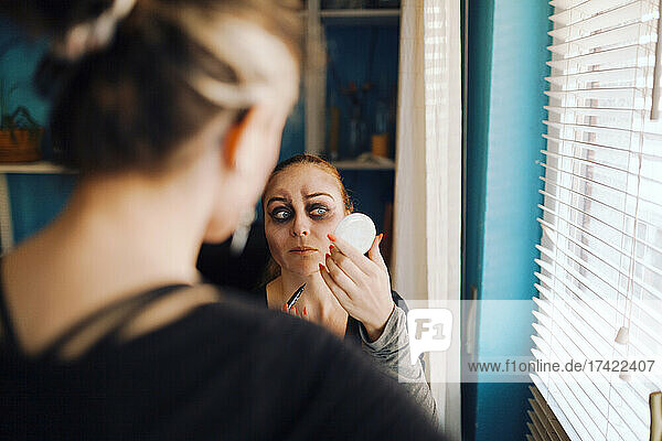 Woman looking at friend doing make-up during Halloween at home