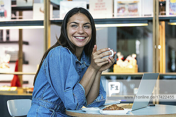 Smiling woman with laptop having coffee at cafe
