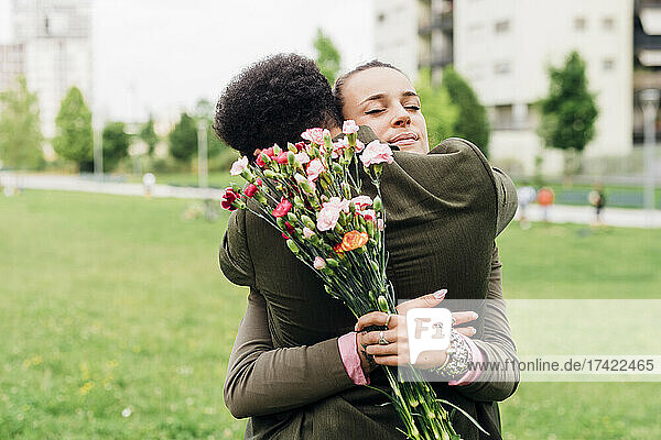Businesswoman holding bouquet while hugging colleague at park