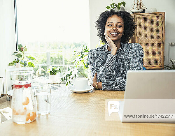 Smiling female professional with hand on chin sitting at desk
