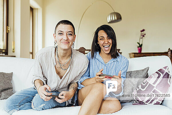 Cheerful young girlfriends playing video games in living room at home