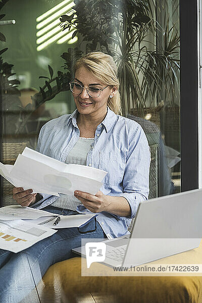 Female freelancer checking documents while sitting with laptop at home