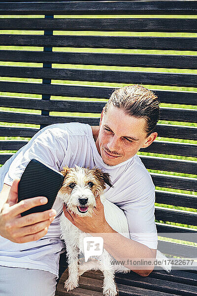 Mann macht Selfie mit Haustier per Handy  während er auf Bank sitzt