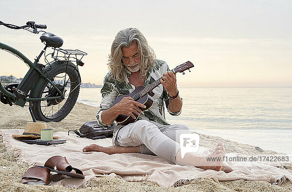Mature man with gray hair playing ukulele at beach