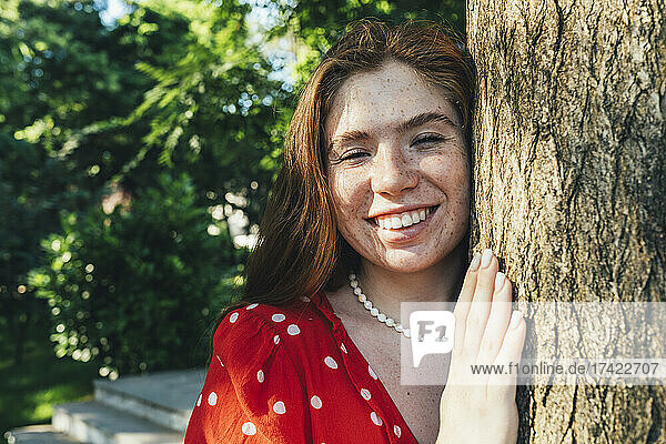 Happy young woman by tree trunk in park