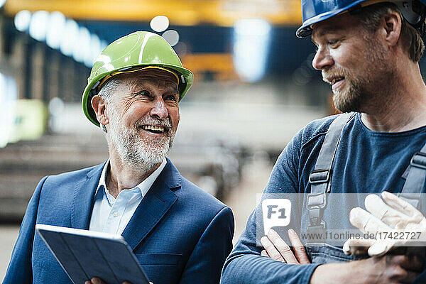 Lächelnder Geschäftsmann diskutiert über digitales Tablet in der Metallindustrie
