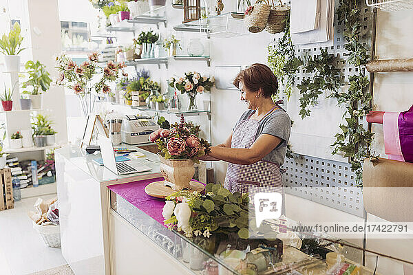 Female entrepreneur with short hair arranging flowers while working in shop