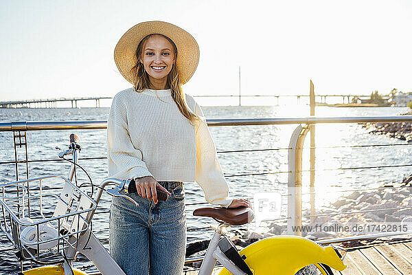 Smiling woman standing with bicycle on boardwalk