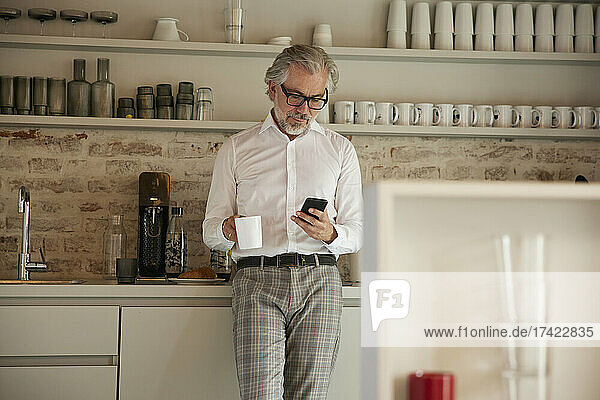 Geschäftsmann benutzt Mobiltelefon beim Kaffeetrinken in der Cafeteria