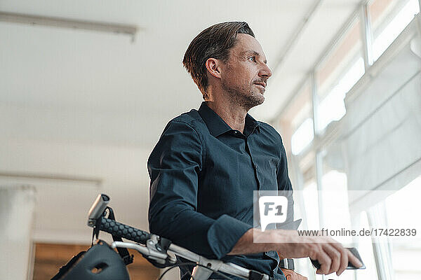 Mature businessman standing with bicycle in office