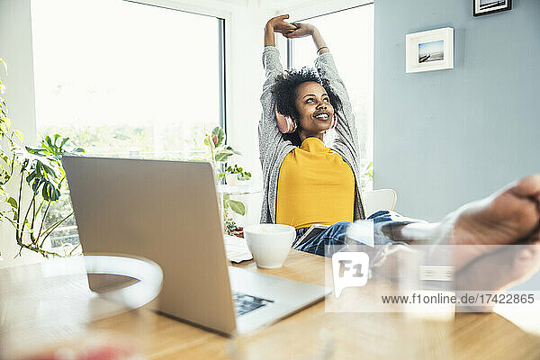 Young businesswoman stretching with arms raised while listening music at home