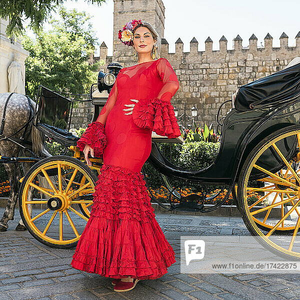 Female dancer wearing flamenco dress standing by horse carriage