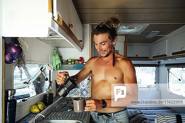 Lächelnder Mann ohne Hemd gießt Kaffee ein  während er im Wohnmobil steht