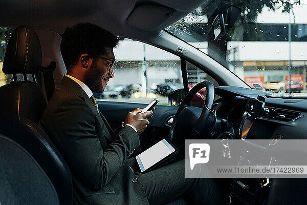 Male professional using mobile phone while sitting with digital tablet in car