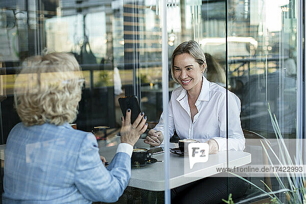 Businesswomen discussing while sitting in cafe seen through glass window