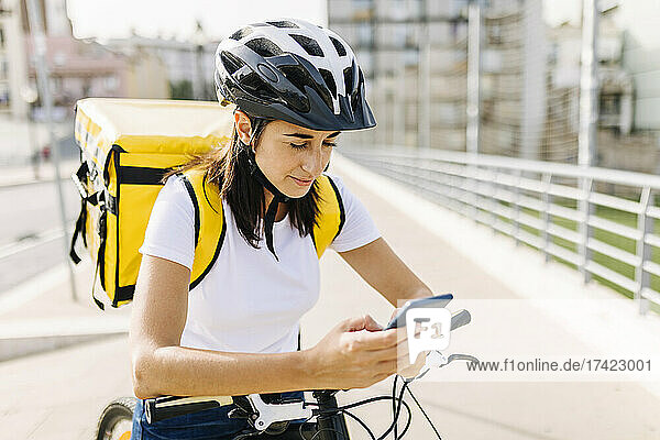 Delivery woman checking mobile phone while standing with bicycle on road