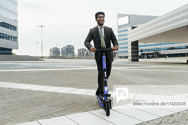 Young businessman riding electric push scooter in city