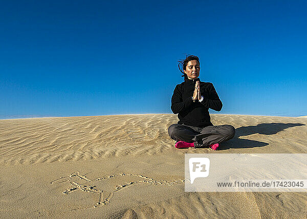 Woman meditating on sand during sunny day