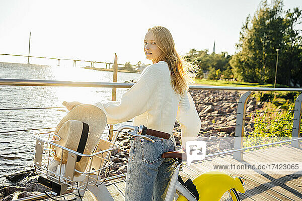 Young blond woman looking over shoulder while standing with bicycle during sunny day