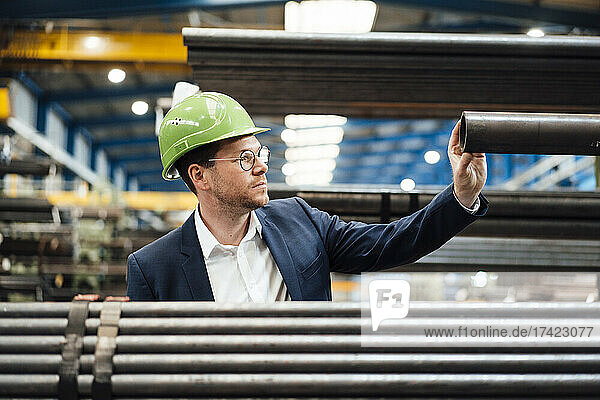 Männlicher Manager trägt Schutzhelm und prüft Rohr während der Arbeit in der Fabrik