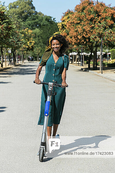 Happy young woman riding electric push scooter during sunny day
