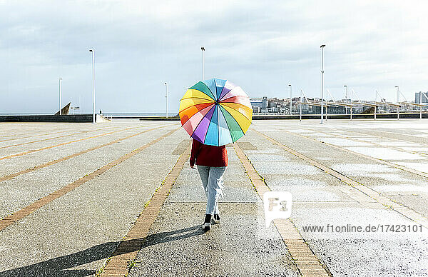 Woman walking with multi colored umbrella on footpath during sunny day