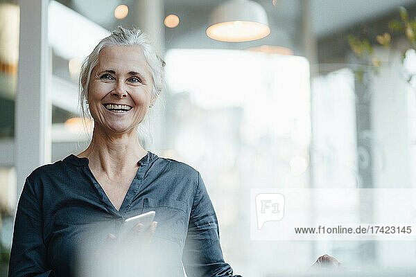 Cheerful female freelancer with mobile phone in coffee shop