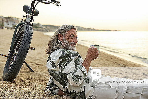Mature man holding mug while relaxing at beach