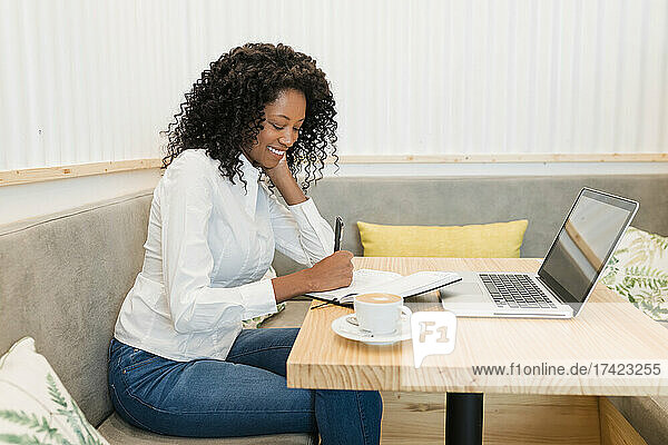Freiberuflerin schreibt in einem Buch  während sie im Café sitzt