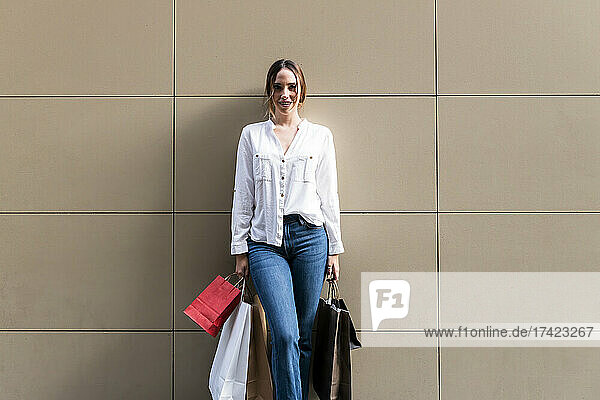 Smiling woman standing with shopping bags against wall