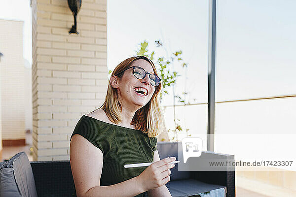 Happy businesswoman with digitized pen sitting on sofa at rooftop