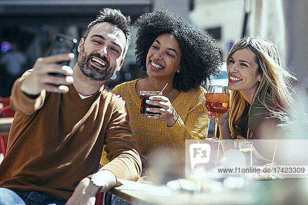 Cheerful man taking selfie with female friends at restaurant