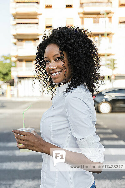 Smiling businesswoman holding juice while standing on road