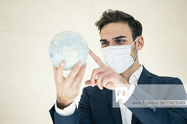 Young male professional touching globe while working in office during pandemic