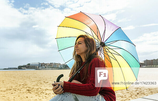 Frau mit Regenschirm träumt  während sie am Strand sitzt