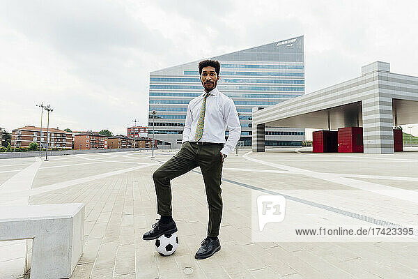 Young businessman standing with soccer ball on footpath