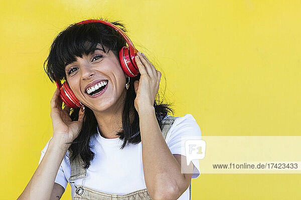 Happy young woman listening music in front of yellow wall