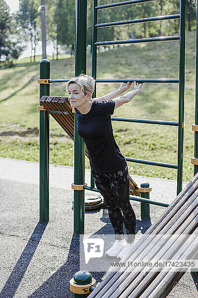 Frau streckt die Hände aus  während sie an einem sonnigen Tag im Park Sport treibt