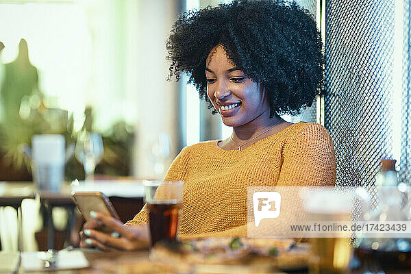 Smiling Afro woman using mobile phone in restaurant