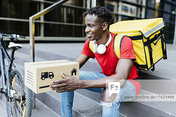 Smiling delivery man with package sitting on steps