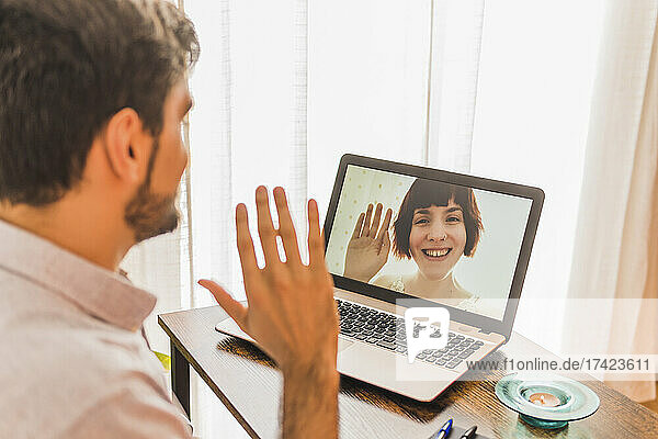 Man greeting woman on video call through laptop at office