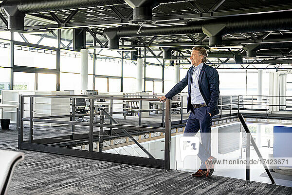 Businessman with hand in pocket standing by railing in office
