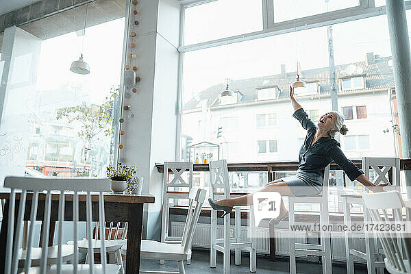 Cheerful businesswoman with arms outstretched sitting in cafe by glass window