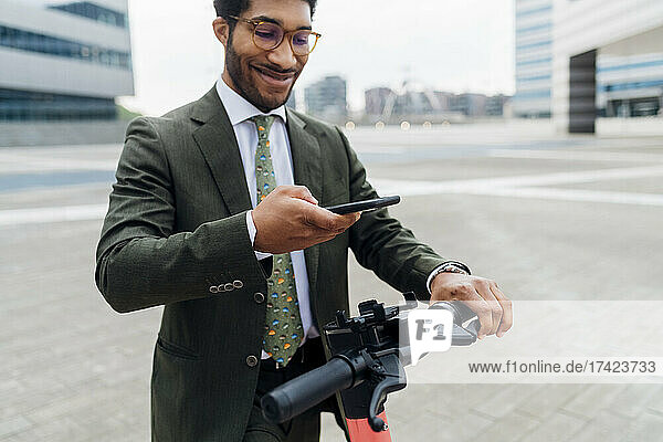 Smiling businessman unlocking electric push scooter through mobile phone