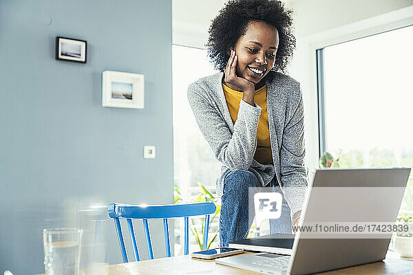 Smiling businesswoman using laptop while leaning on chair at desk