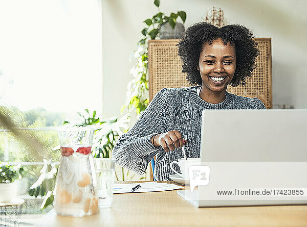 Smiling female professional having coffee during video conference at desk