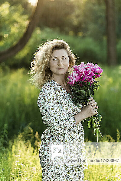 Blond woman with bunch of peonies standing at meadow